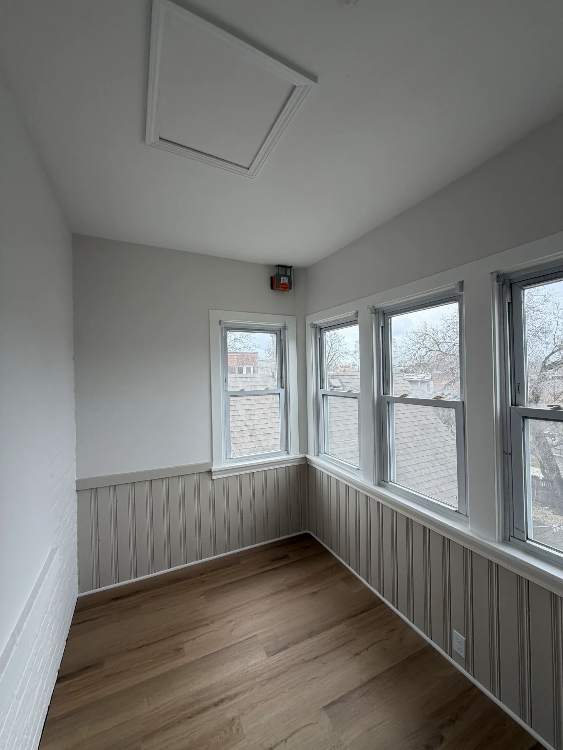 Three-season porch remodel with wood-look LVP flooring, corner windows, and beadboard wainscoting in Chicago two-flat renovation