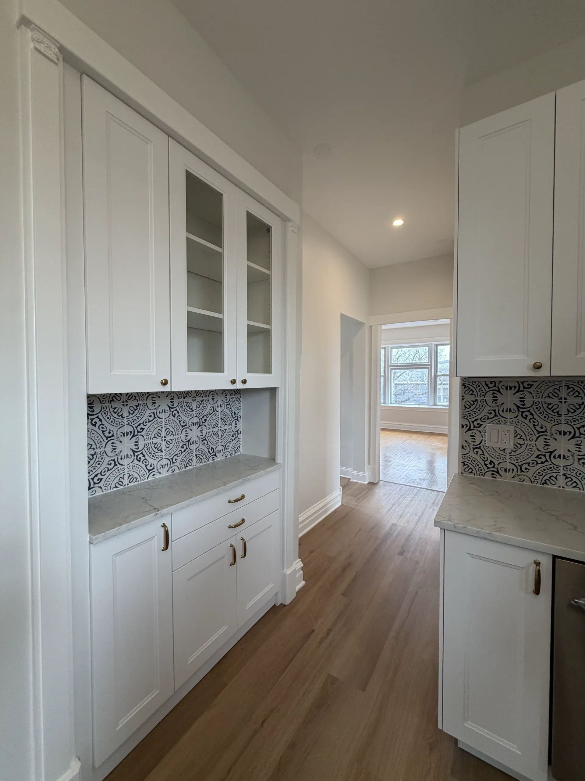 White shaker butler's pantry with quartz countertop, Moroccan encaustic tile backsplash, glass-front upper cabinets, and brass hardware in Chicago kitchen remodel