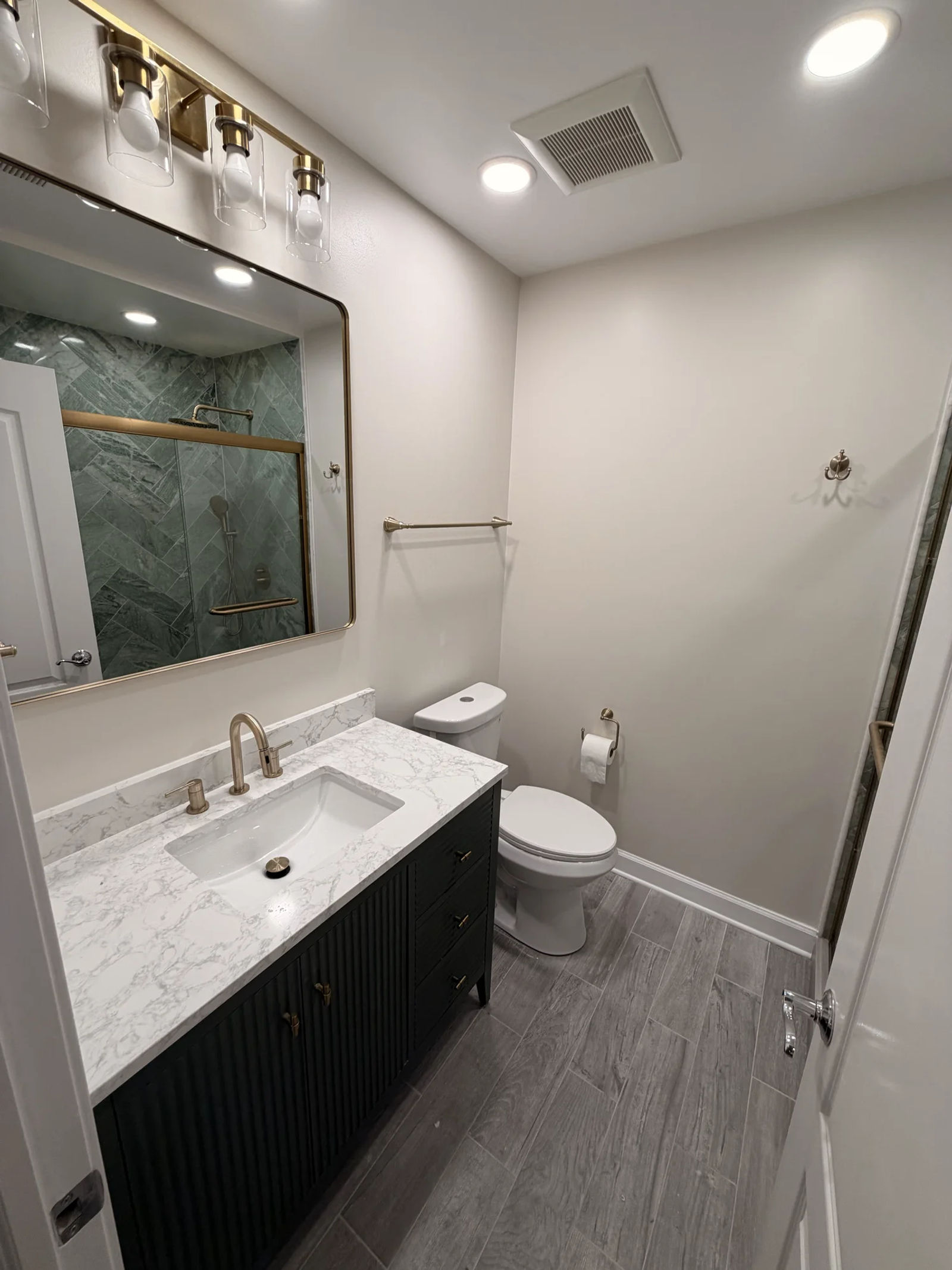 After -- rebuilt guest bathroom with black fluted vanity, marble-look quartz, brass fixtures and green marble shower