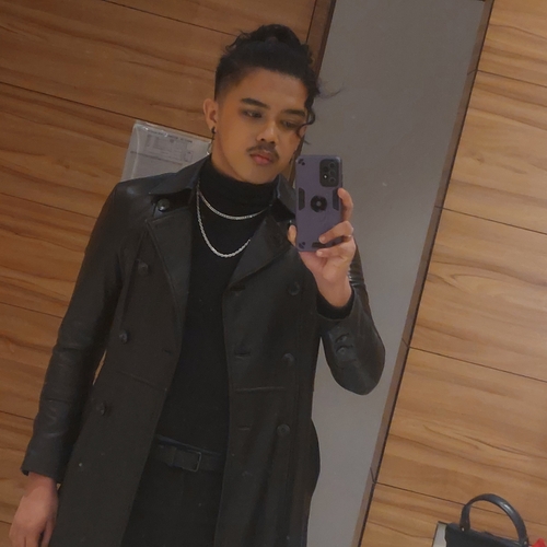 A mirror selfie of me  wearing a black faux-leather coat on top of a black turtleneck and two silver chain necklace.