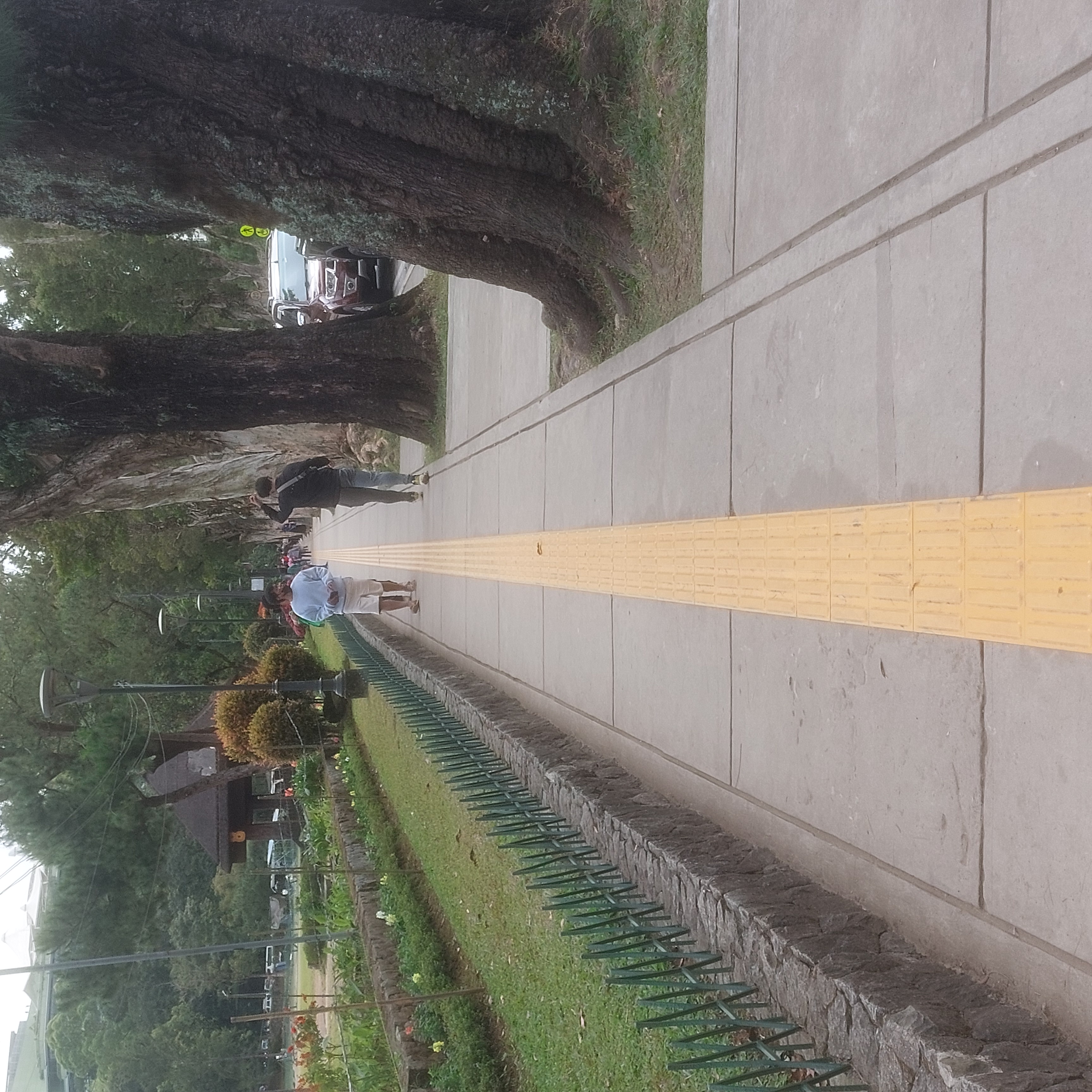A yellow line painted on a sidewalk. People walk past each other.