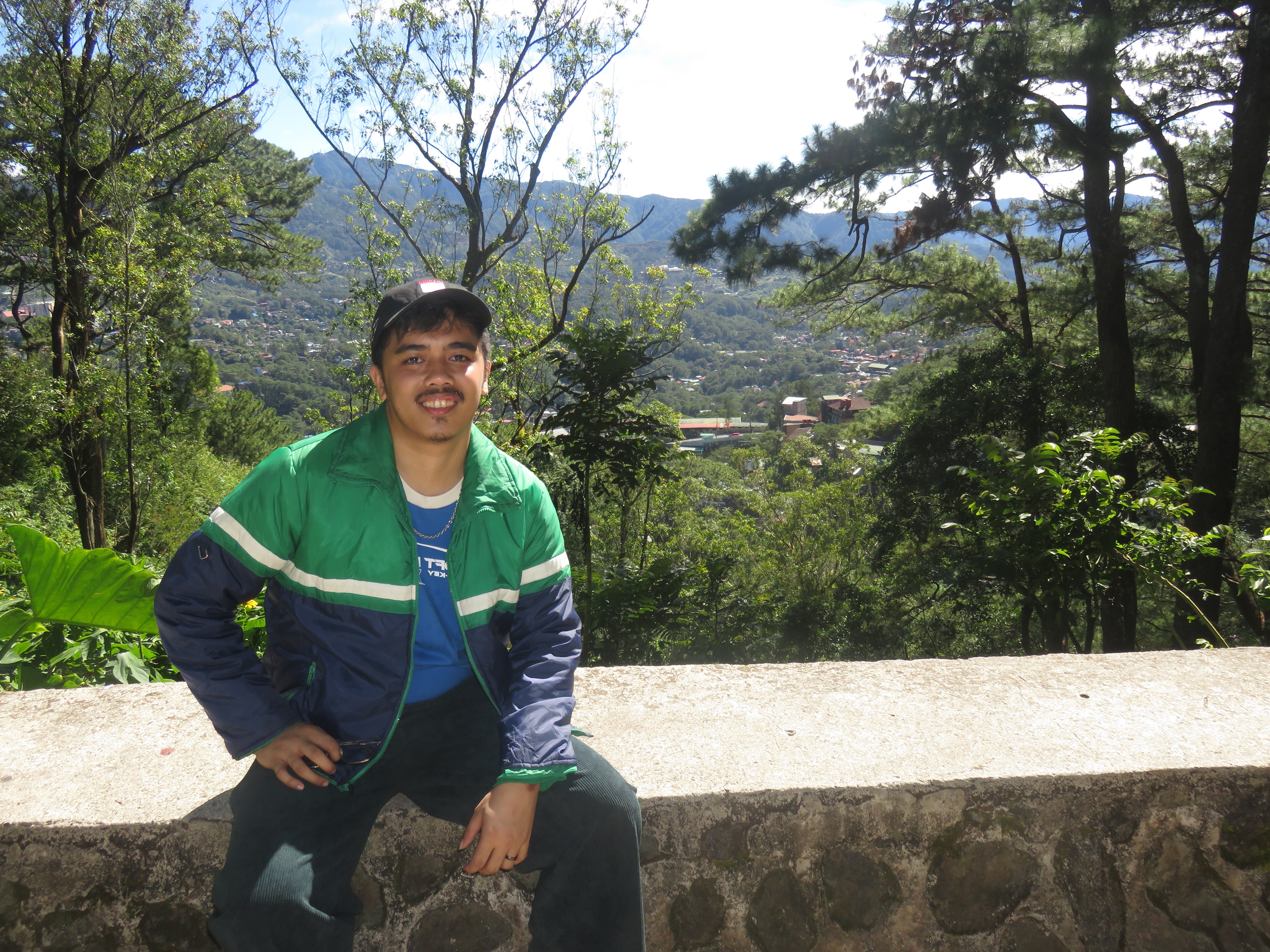 Me in a green jacket sitting on a stone bench overlooking a cliff.