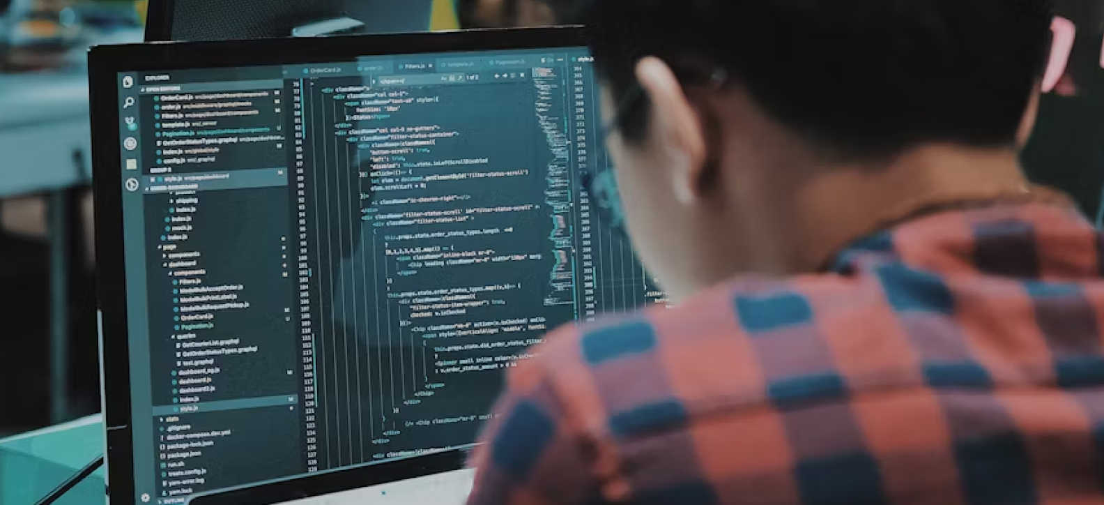 A person wearing a checkered shirt is working on code displayed on a laptop screen.