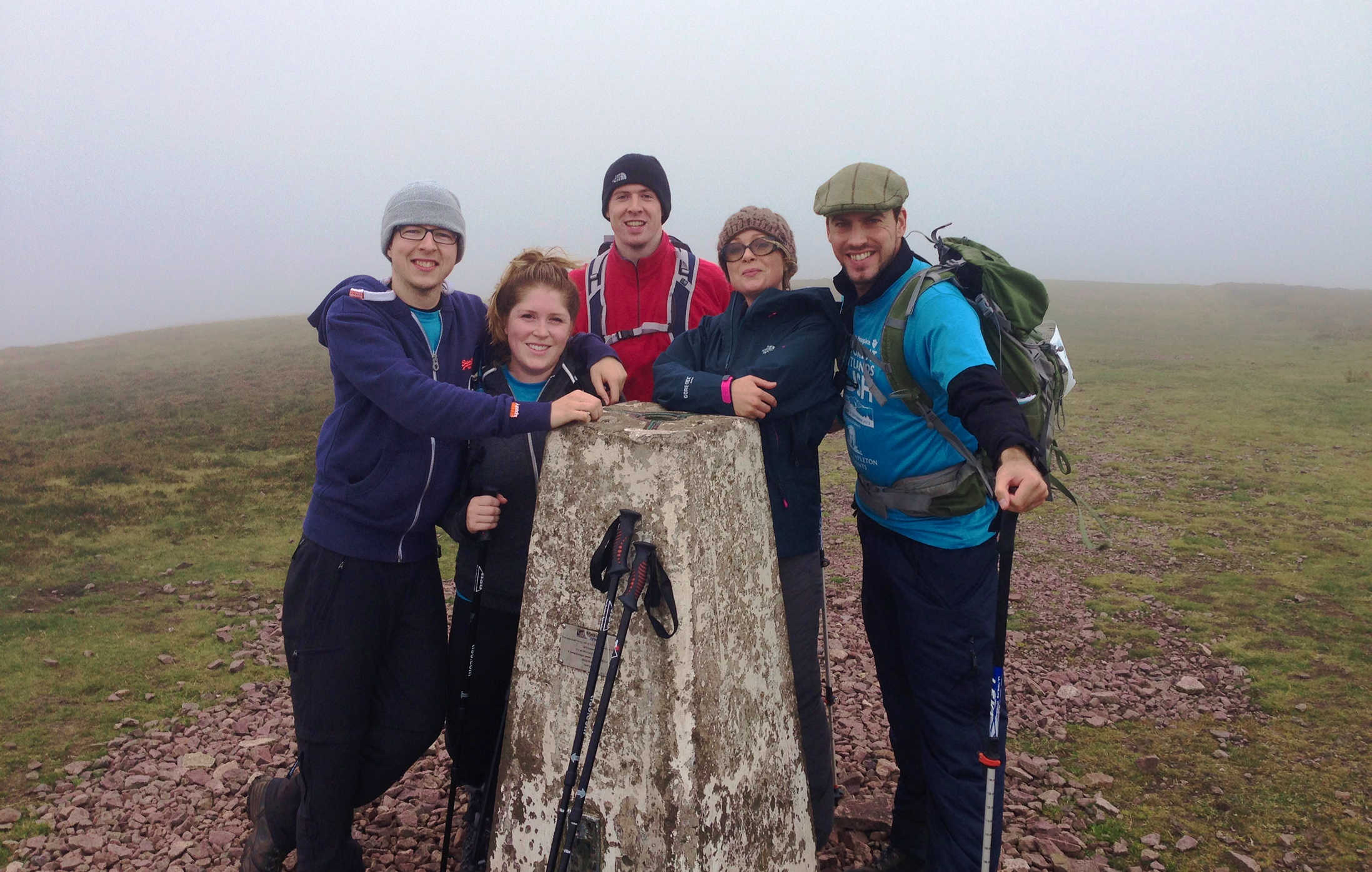 Team 8MS standing at a trig point on a hilltop in foggy conditions.