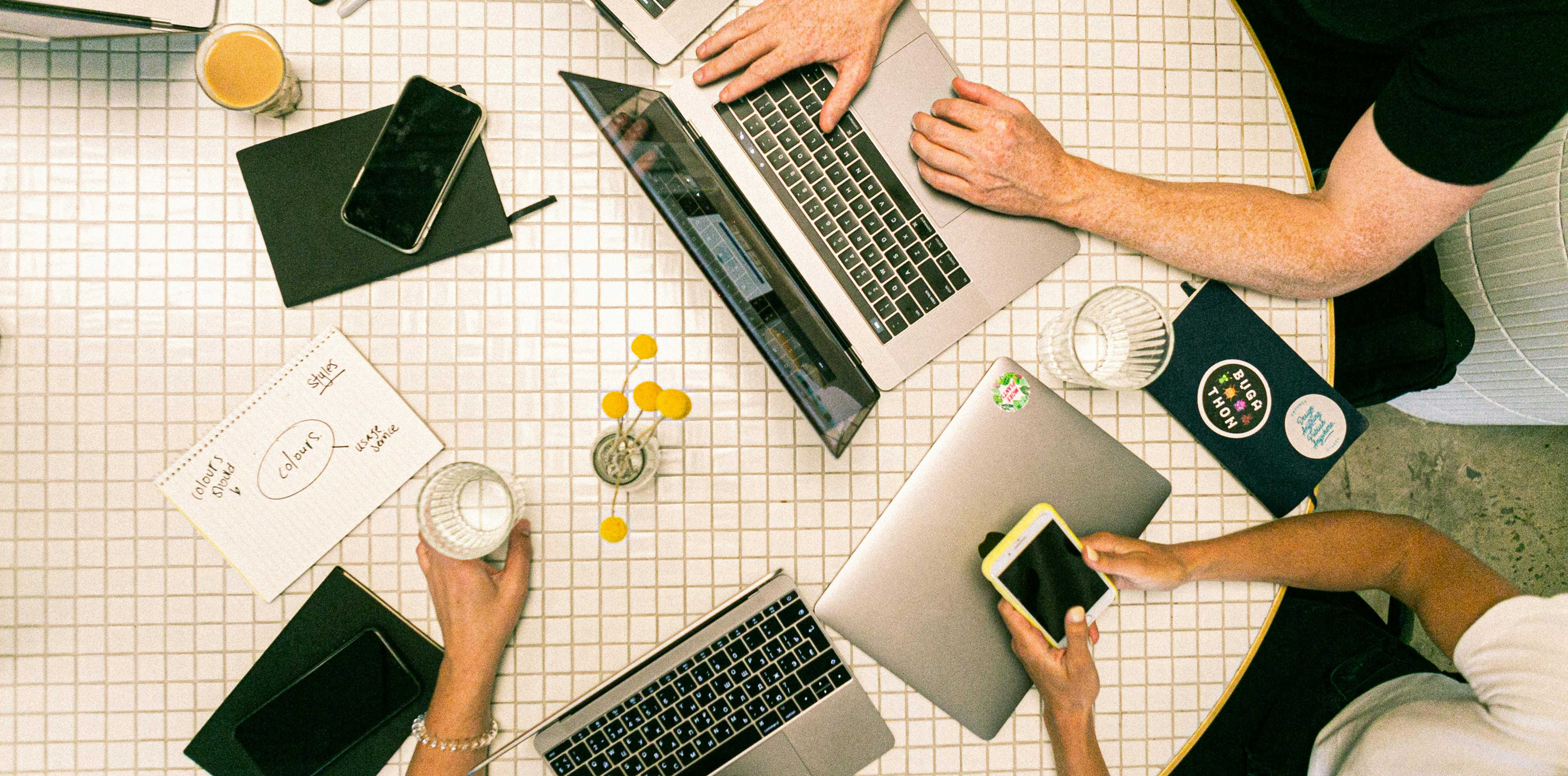 An overhead view of a tiled table which has numerous laptops, both open and closed on top.