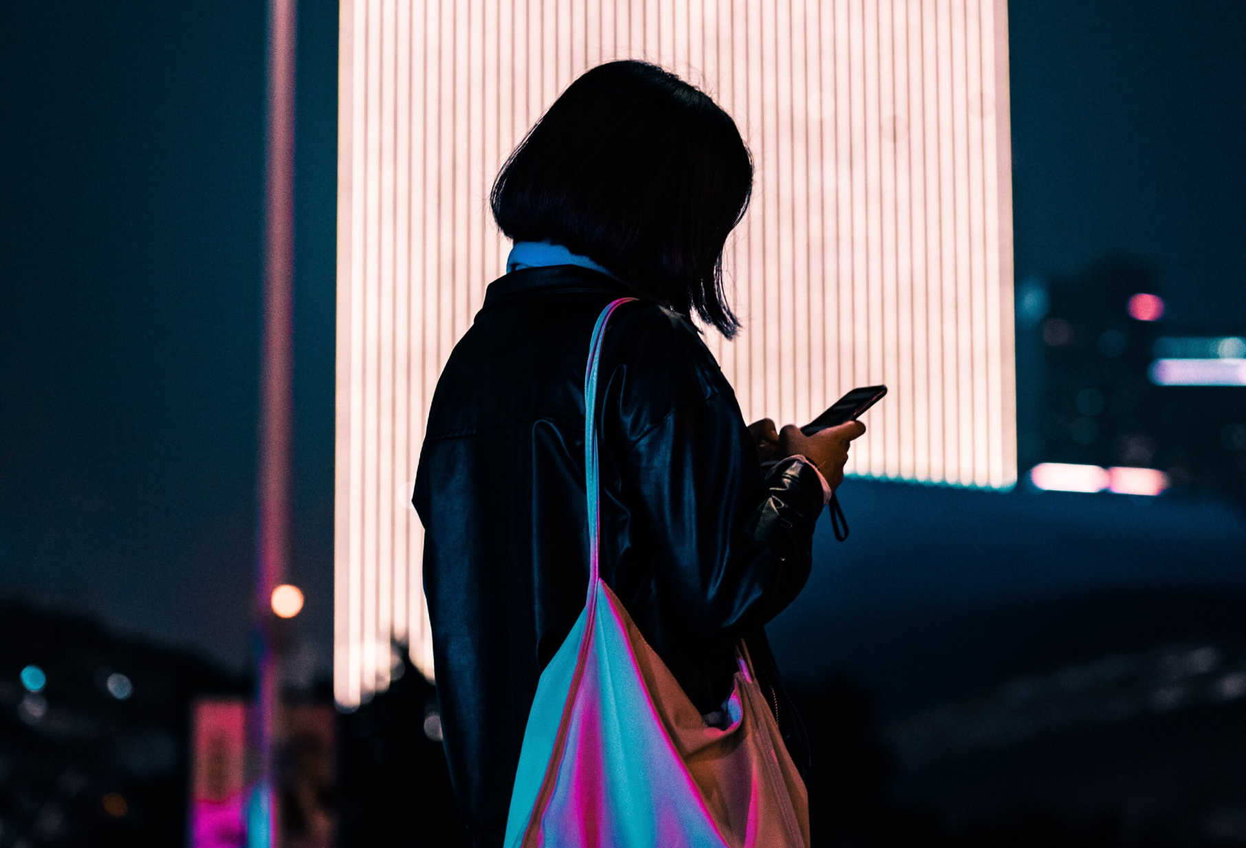 A woman standing outdoors at night, looking at her phone.