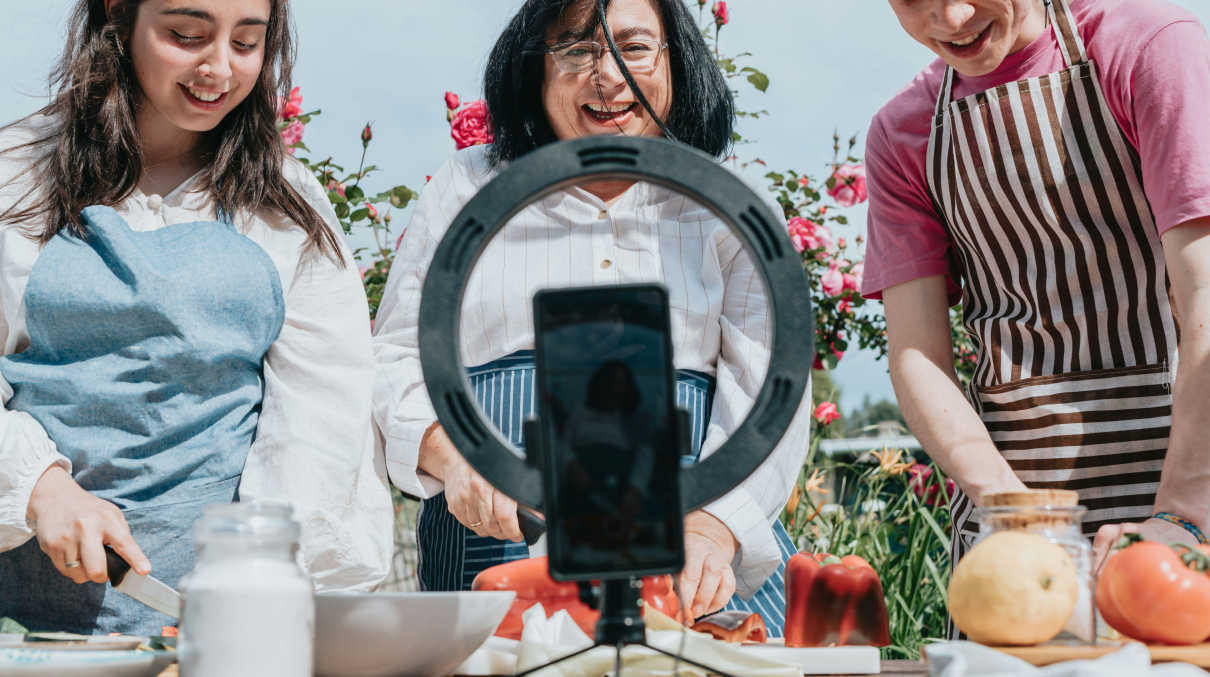 Three people chopping vegetables with a phone filming and a ring light surrounding the phone.