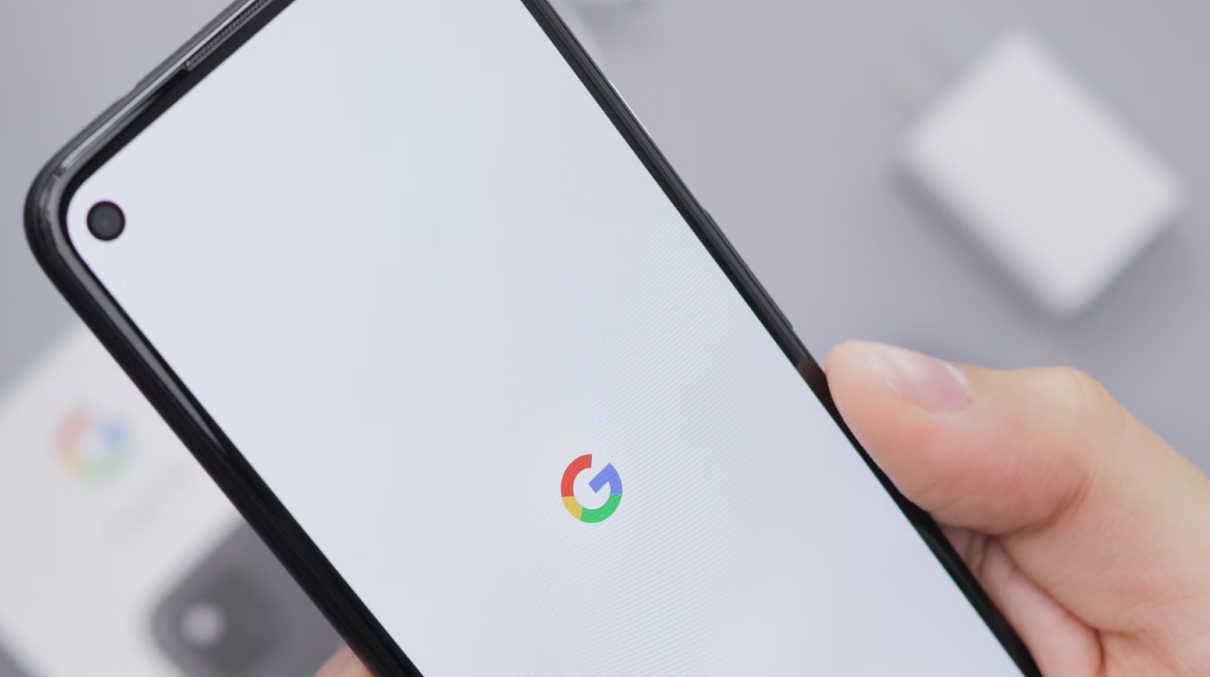 A hand holding a phone with the Google logo on the screen.