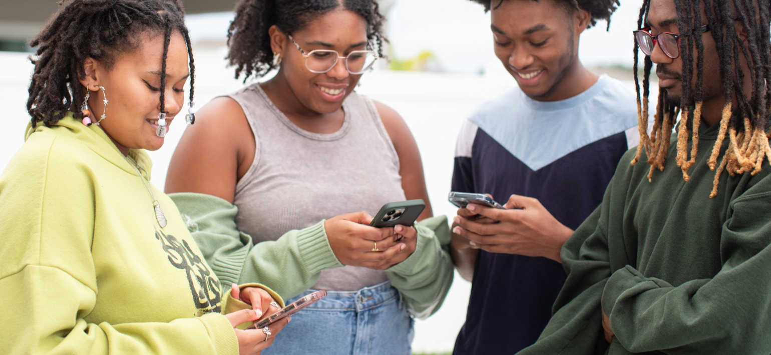 Four people standing in a group, with three of them looking at their phones.
