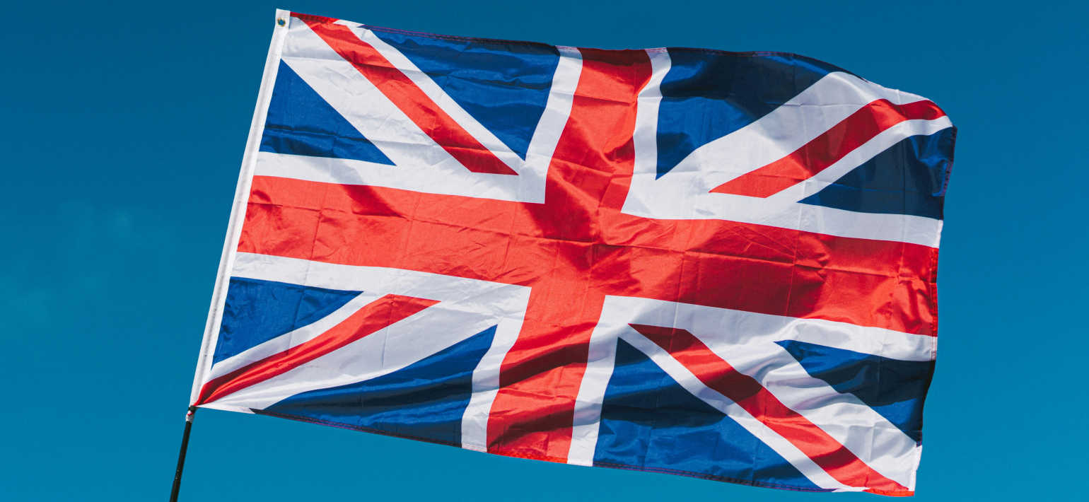 Union Jack flying in the wind against a blue sky background.
