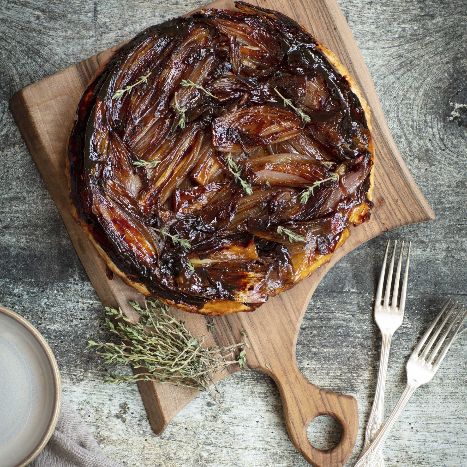 Overhead shot of a caramelised onion tart on a wooden chopping board.