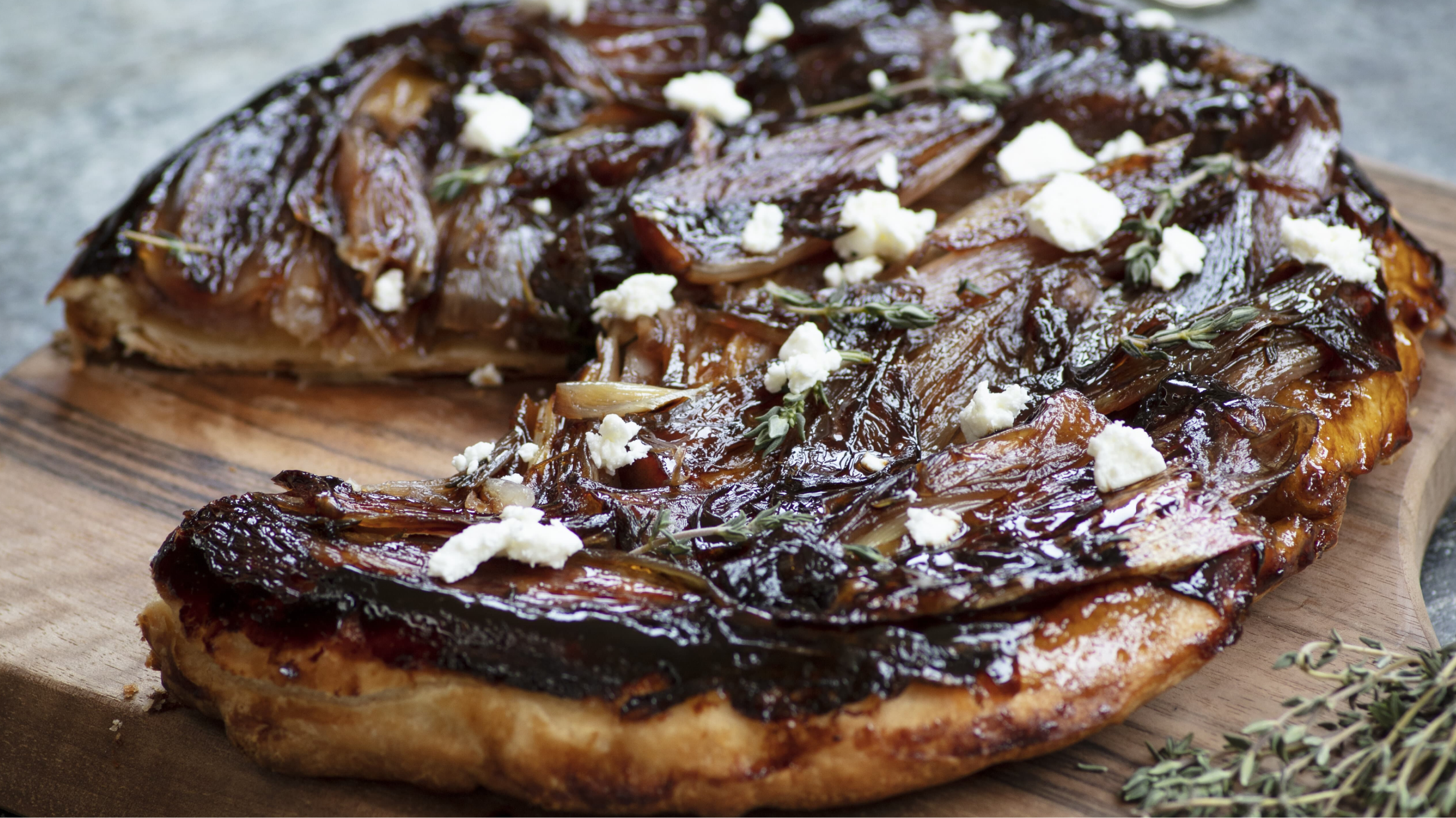 Close up of a caramelised onion tart with crumbles of feta, on a wooden chopping board.