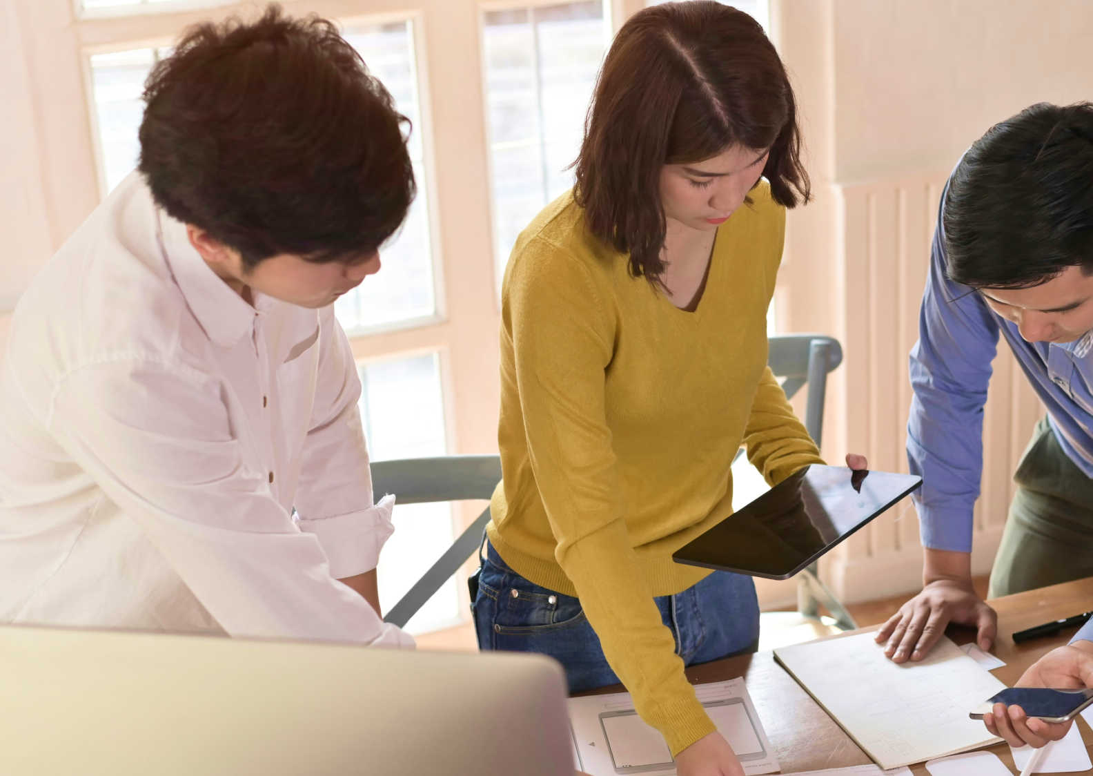Three people collaborating at a desk, reviewing documents and information on a tablet.