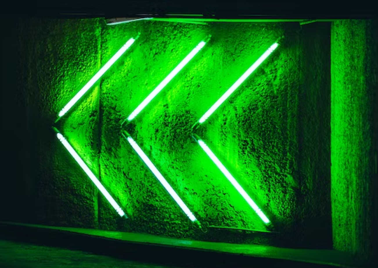 Three green neon arrow shapes pointing left on a textured wall.