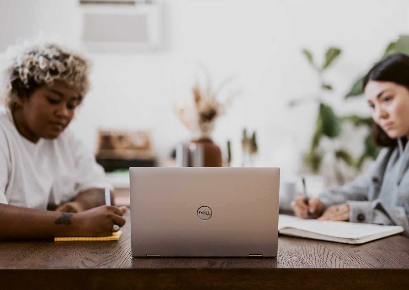 Two people sitting at a desk looking at a shared laptop and taking notes.