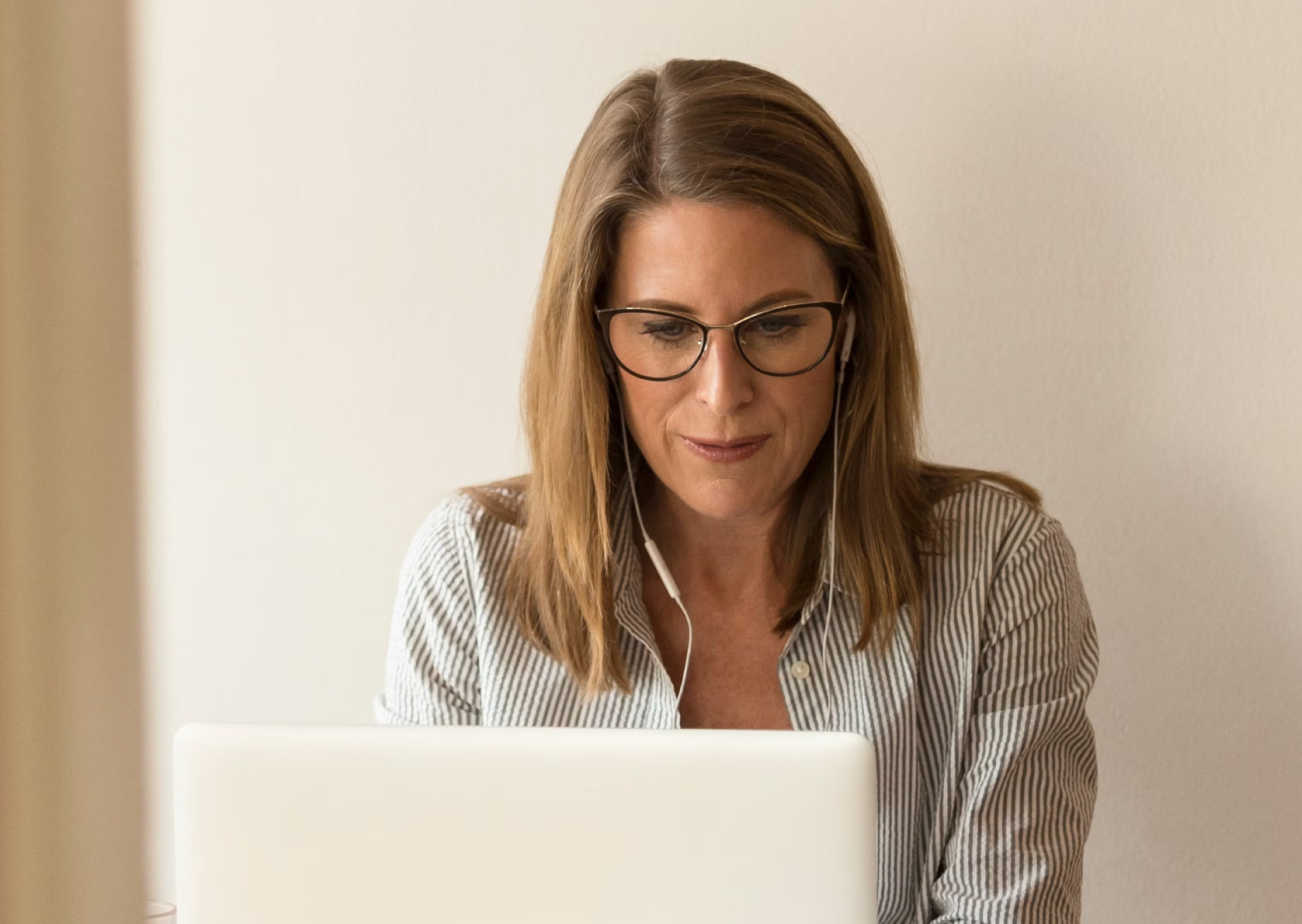 A woman working on a laptop with earphones plugged in.