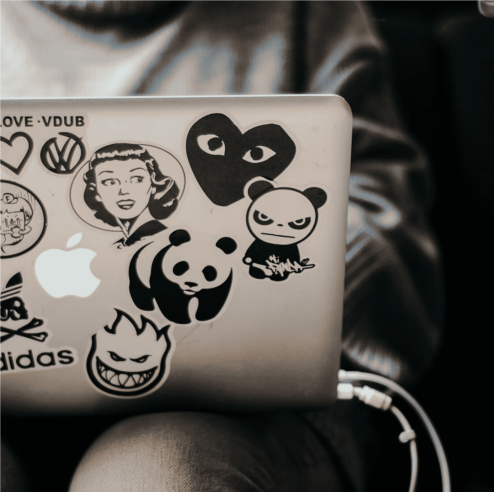 A laptop covered in various black-and-white stickers, including pandas, logos, and cartoon faces.