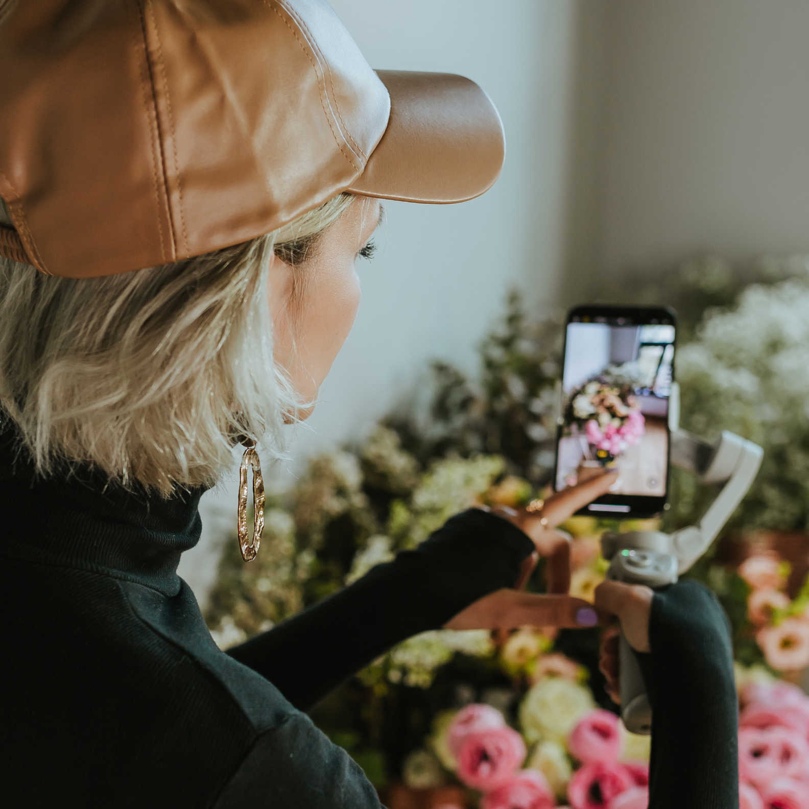 A woman using a smartphone on a gimbal to film a bouquet of flowers.