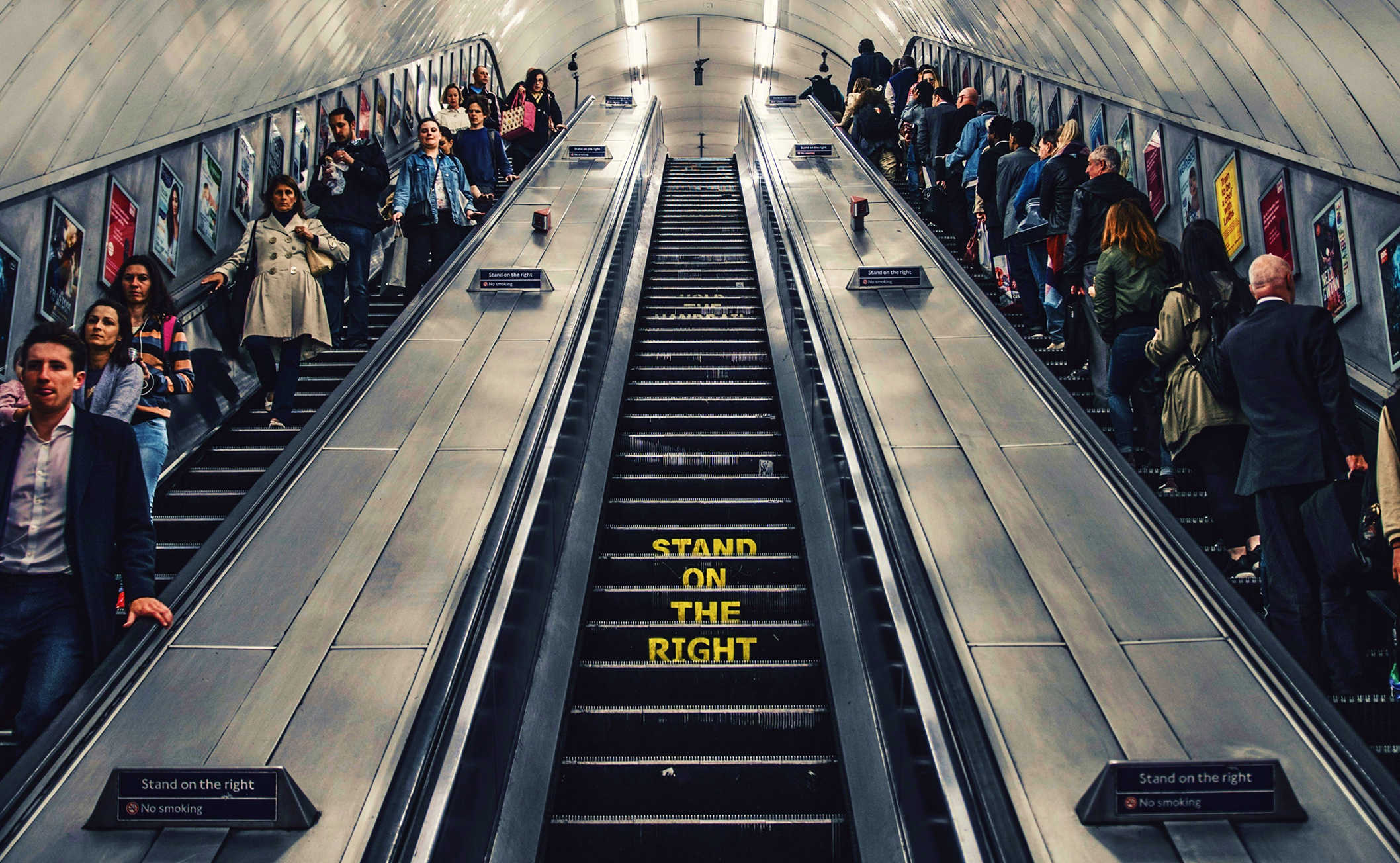 An escalator in an underground station, with people standing on the right side and walking on the left.