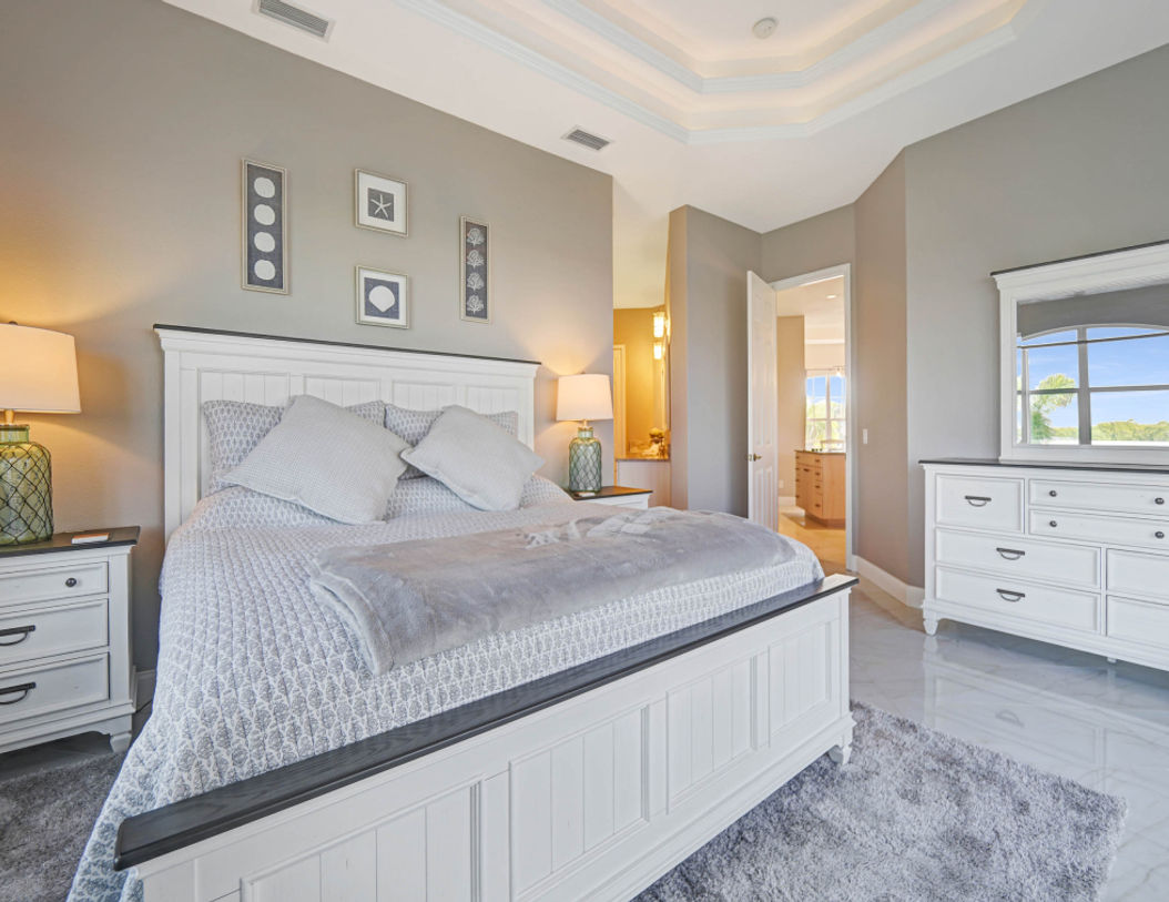 Big Bed Covered in White and Gray Bedding With Table and Lamp on Top