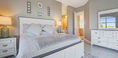 Big Bed Covered in White and Gray Bedding With Table and Lamp on Top