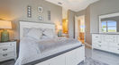 Big Bed Covered in White and Gray Bedding With Table and Lamp on Top