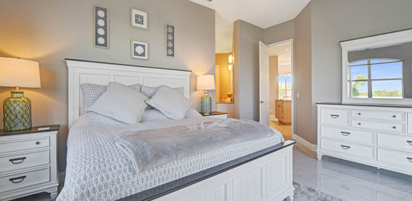 Big Bed Covered in White and Gray Bedding With Table and Lamp on Top
