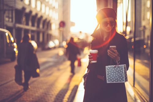 A happy customer with a hot beverage in one hand and a phone and gift bag in the other.