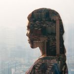 A female business employee thinking about business communication while looking at buildings outside through the glass.