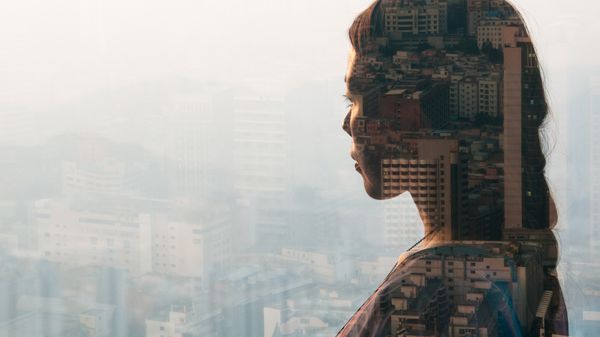 A female business employee thinking about business communication while looking at buildings outside through the glass.