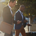 3 professionals in suits using 8x8 UCaaS on smartphones as they walk across a square