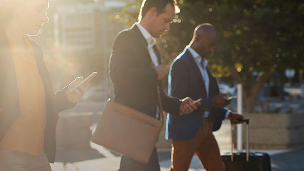 3 professionals in suits using 8x8 UCaaS on smartphones as they walk across a square