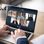 An office employee using 8x8 work on his laptop to connect with and see his five colleagues via video call