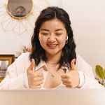 A smiling woman with 2 thumbs up in front of a computer