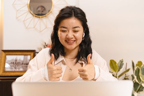 A smiling woman with 2 thumbs up in front of a computer