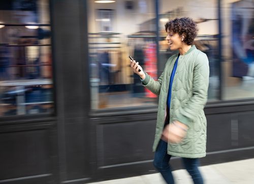 Woman walking on sidewalk checking 8x8's service status on her phone