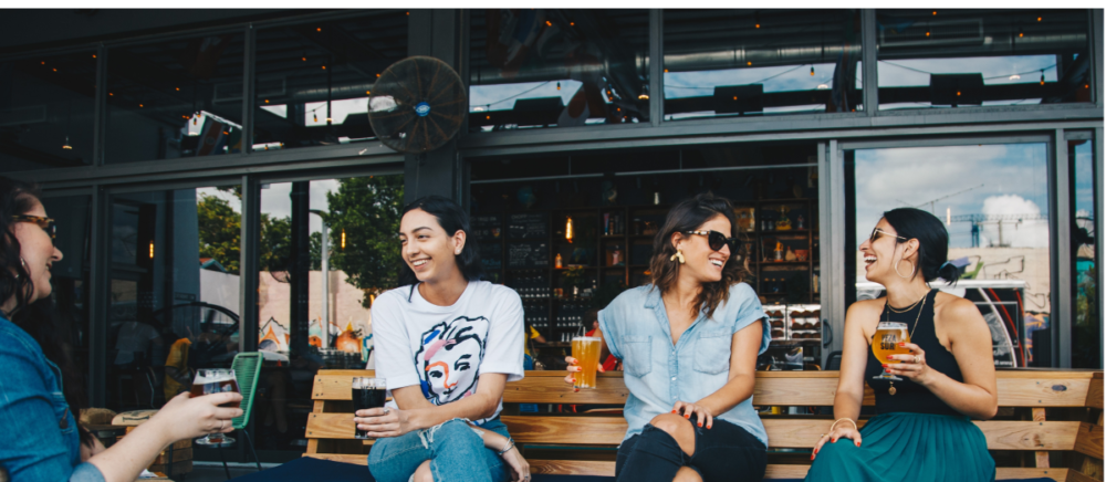 Four young ladies drink beer and laugh.