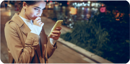 A young girl is looking at her smartphone in the street.