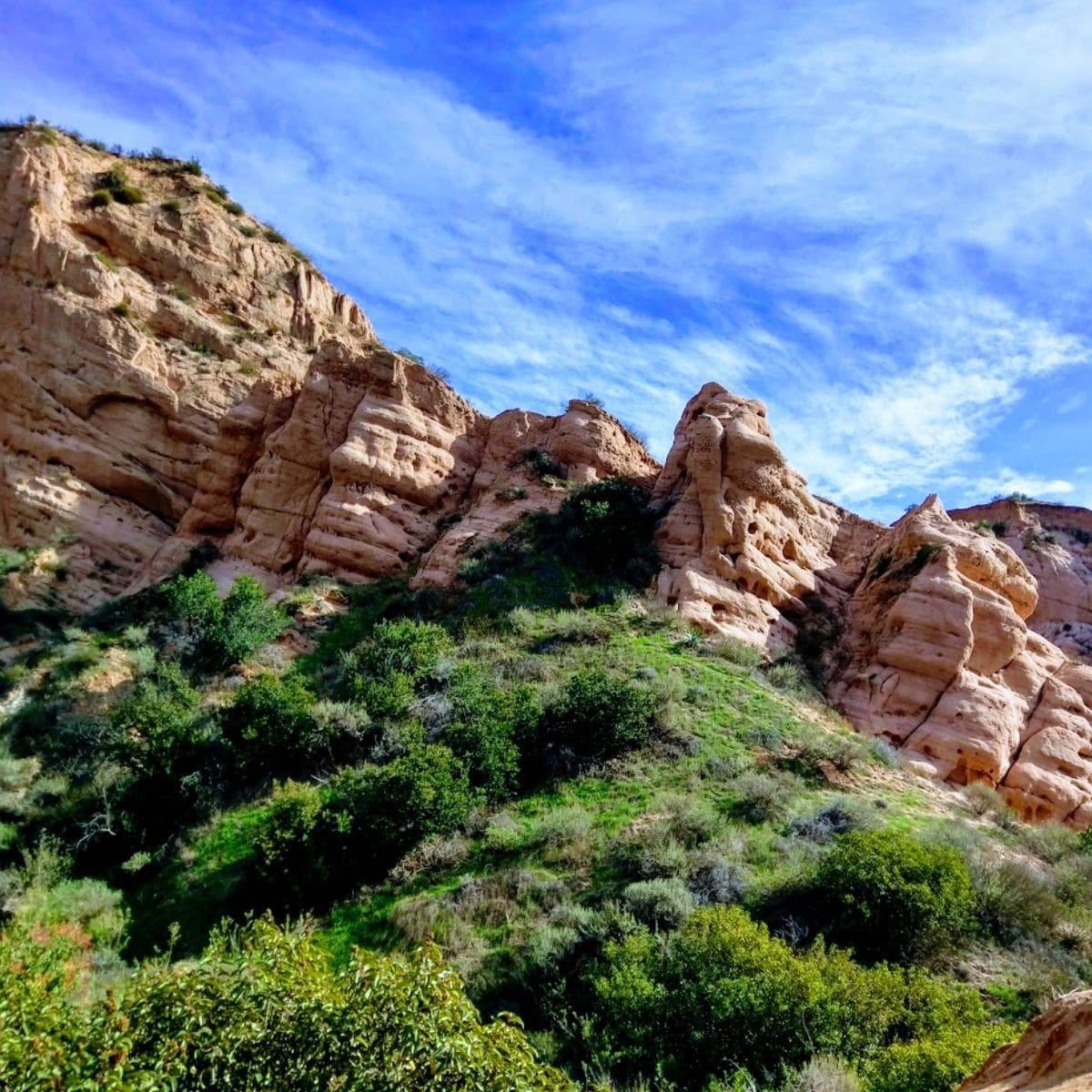 Dramatic sandstone rock formations rising above dense green vegetation beneath a bright blue sky near Foothill Ranch, California.