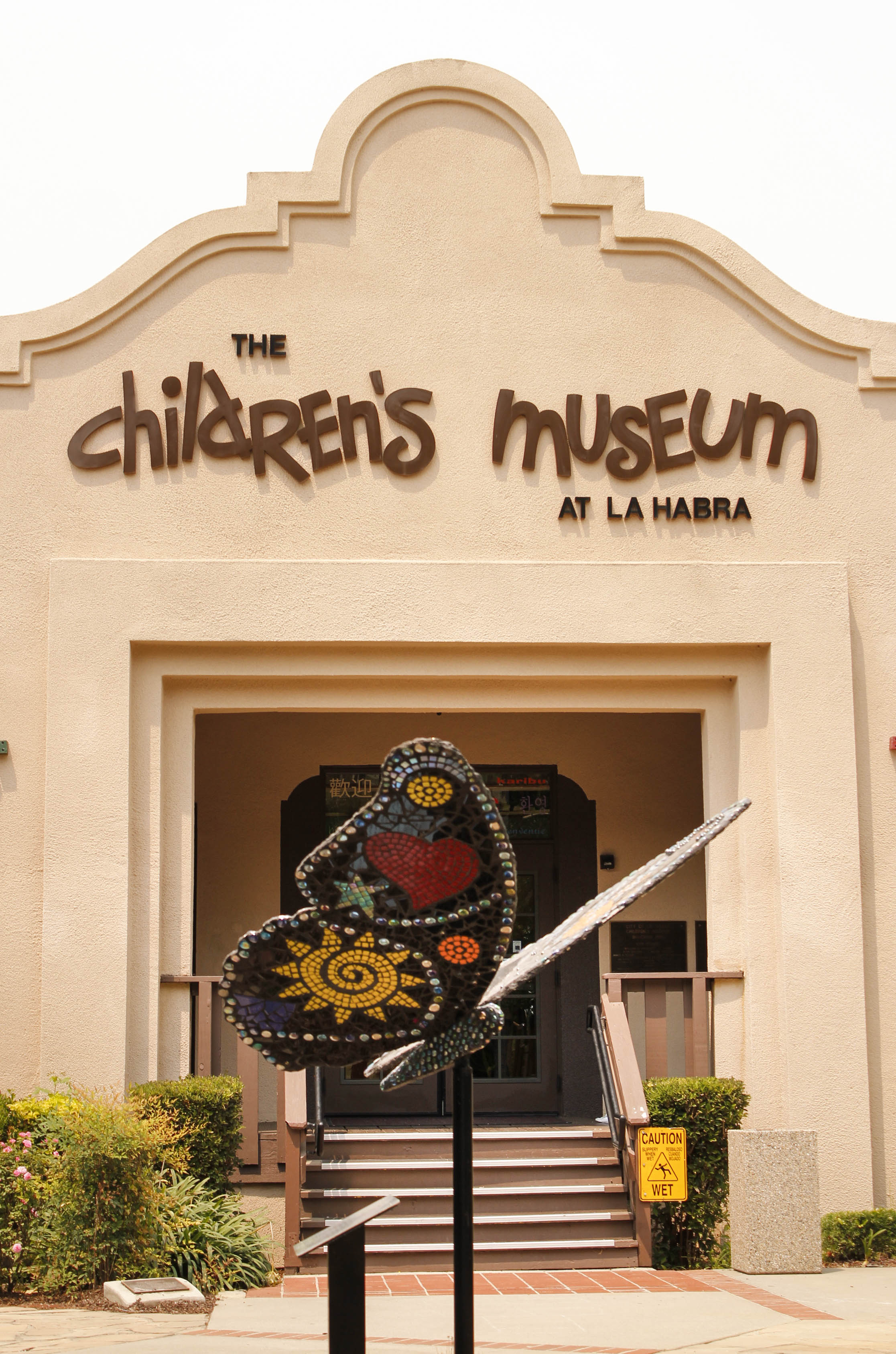 Entrance to the Children’s Museum at La Habra in California, featuring its distinctive Spanish-style facade and a colorful mosaic butterfly sculpture displayed outside.