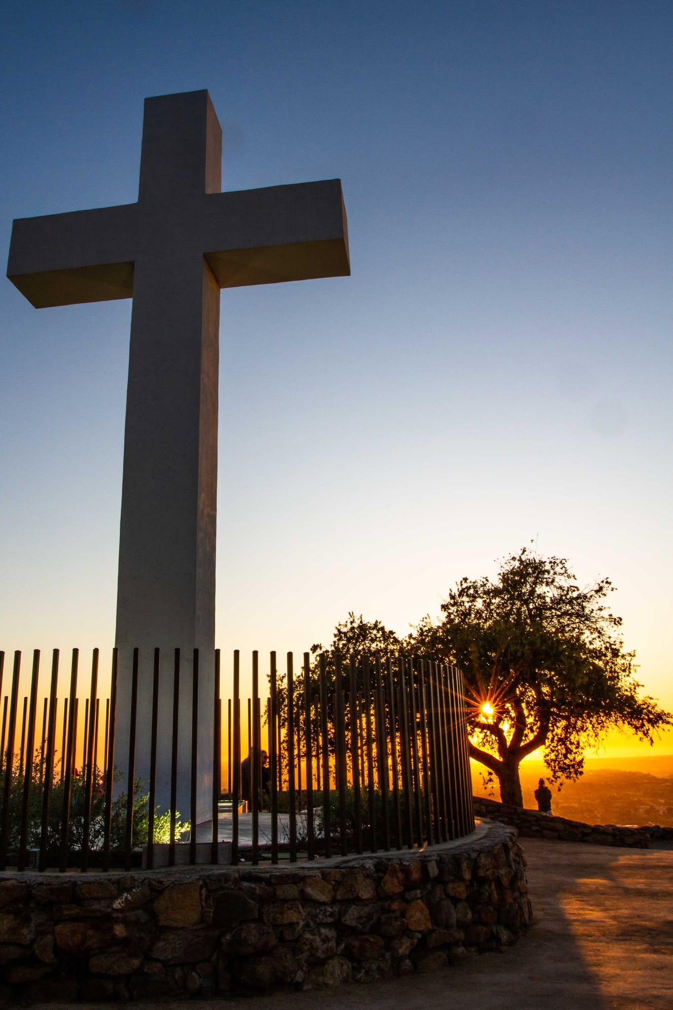 Mount Helix Park cross overlooking the La Mesa, California, area at sunset, with trees, hillside scenery, and warm evening light across San Diego County.