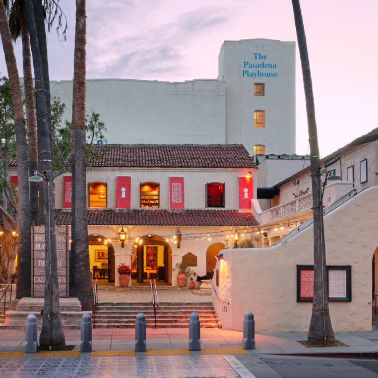 Exterior of The Pasadena Playhouse in Pasadena, California, featuring its historic Spanish Colonial Revival architecture, palm trees, courtyard entrance, and theater signage.