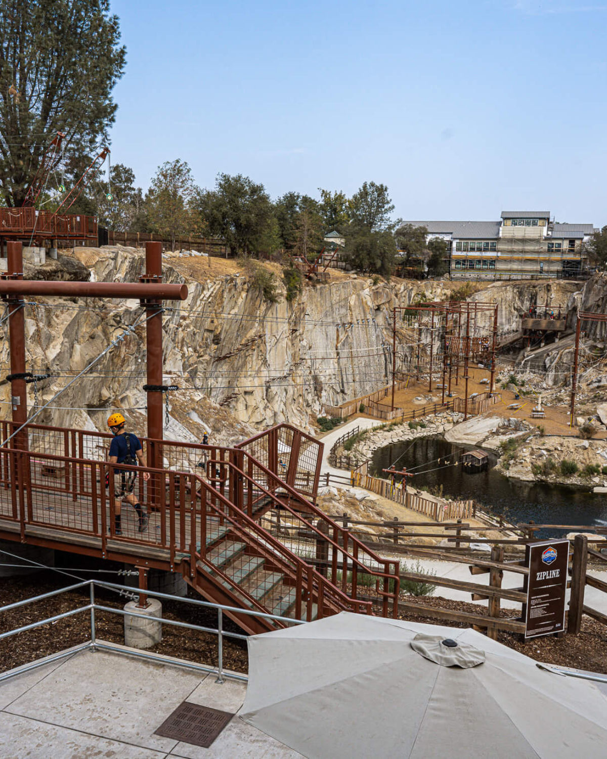 View of Quarry Park in Rocklin, California, showing elevated walkways and ropes-course structures built along the edges of a rocky quarry, with a small pond at the bottom and trees and buildings in the background.