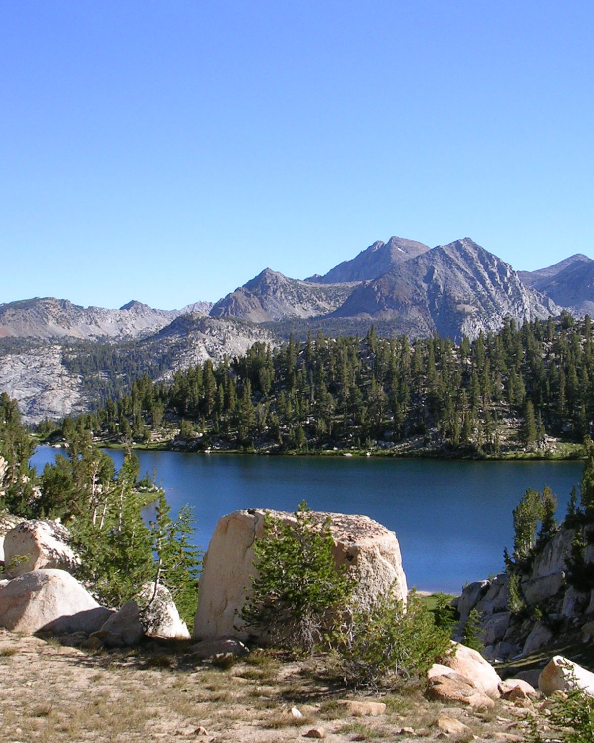 Serene mountain lake surrounded by dramatic granite peaks and lush pine forest in the Sierra Nevada foothills near Tollhouse, CA