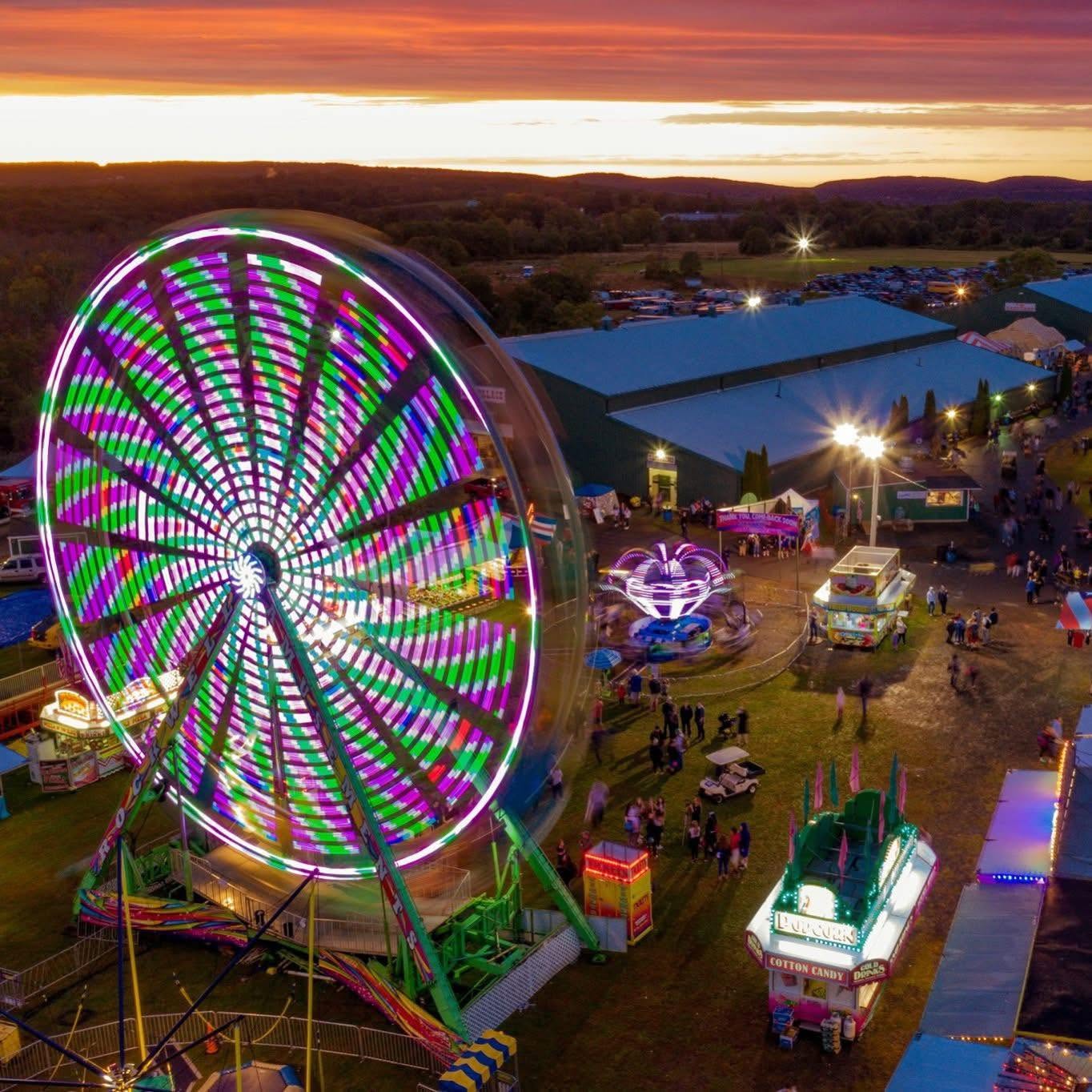 Aerial view of the Durham Fair at sunset, showcasing a brightly lit Ferris wheel, carnival rides, food vendors, fairgrounds, and crowds enjoying one of Connecticut's most beloved annual events.