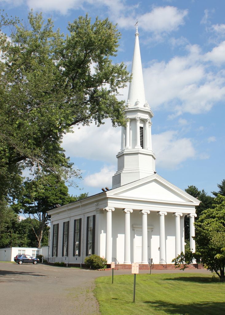 Historic white church in Enfield, CT featuring tall columns, a prominent steeple, and surrounding greenery under a partly cloudy sky