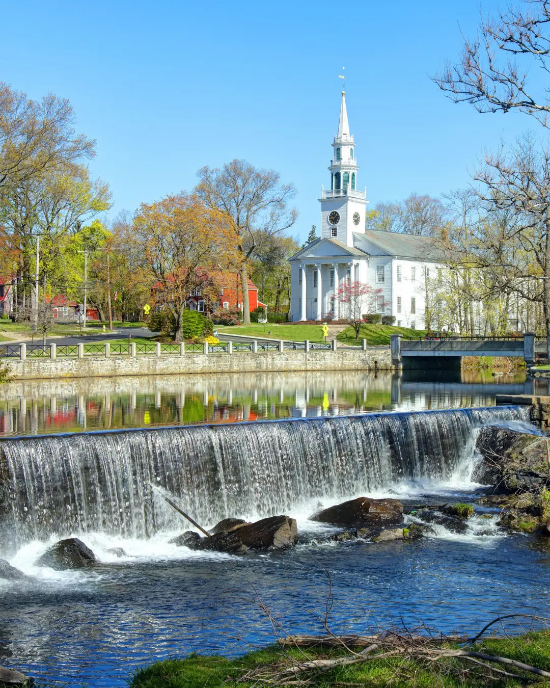View of the Wepawaug River and First United Church of Christ in downtown Milford, Connecticut, featuring a cascading waterfall, historic architecture, and reflections along the river.