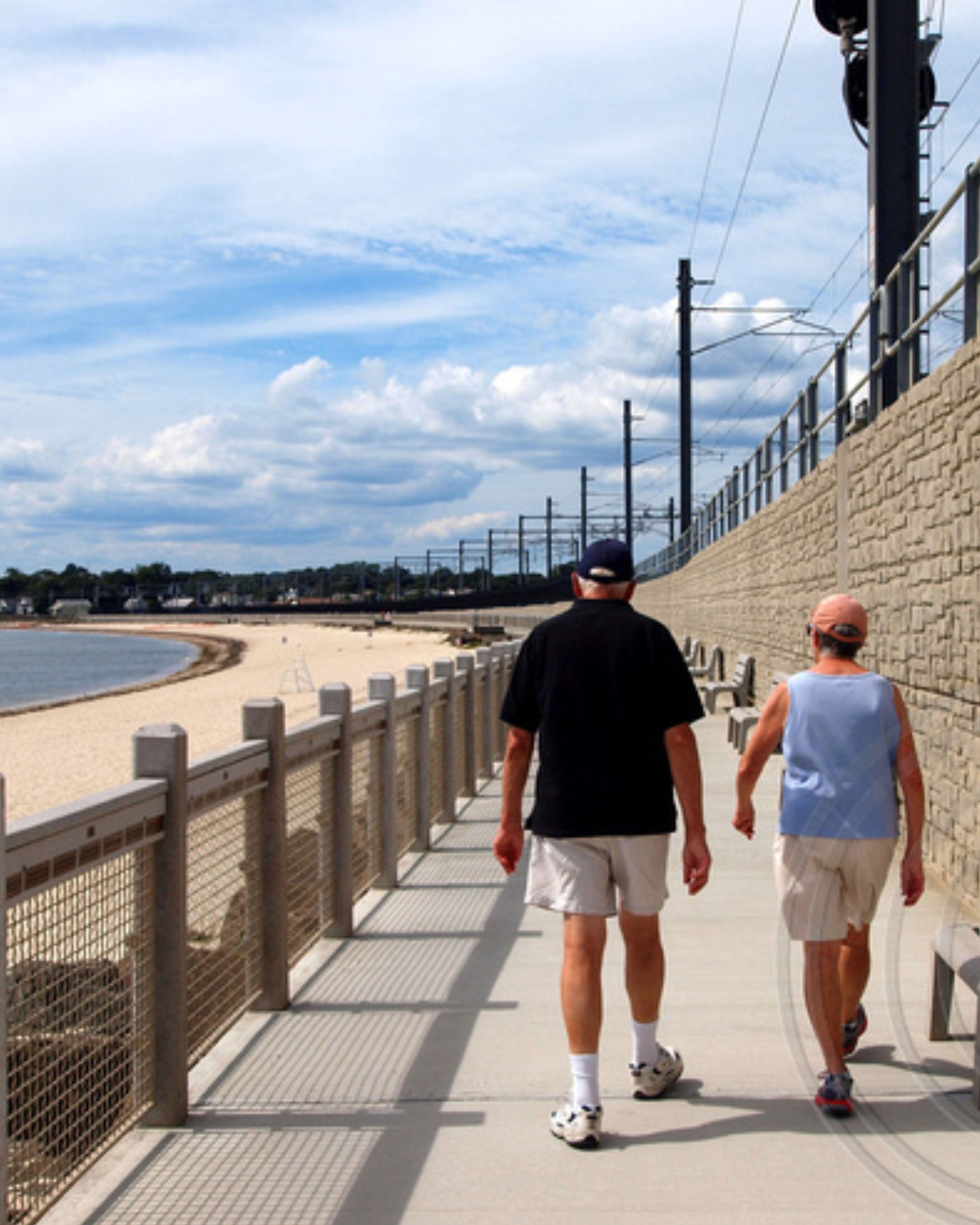 Couple walking along the Niantic Bay Boardwalk in Connecticut, featuring scenic waterfront views, sandy shoreline, and peaceful coastal surroundings.