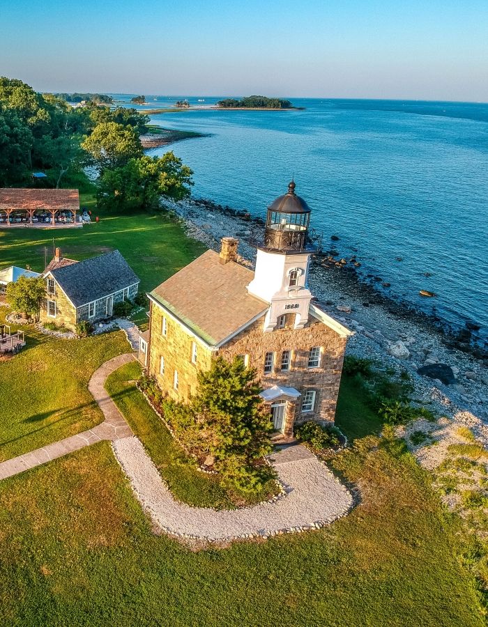 The historic Sheffield Island Lighthouse off the coast of Norwalk, Connecticut. The stone lighthouse stands on a grassy shoreline overlooking Long Island Sound, showcasing its classic lighthouse tower, stone architecture, and coastal New England character.