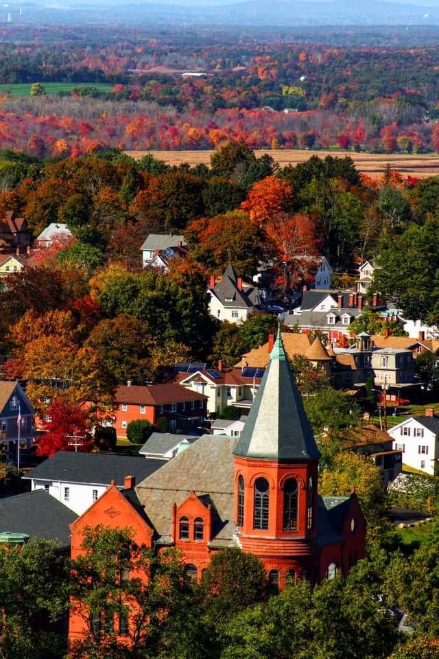 Aerial view of Rockville's historic residential neighborhoods in Vernon, Connecticut, featuring a prominent red brick church with a bell tower surrounded by vibrant New England fall foliage.